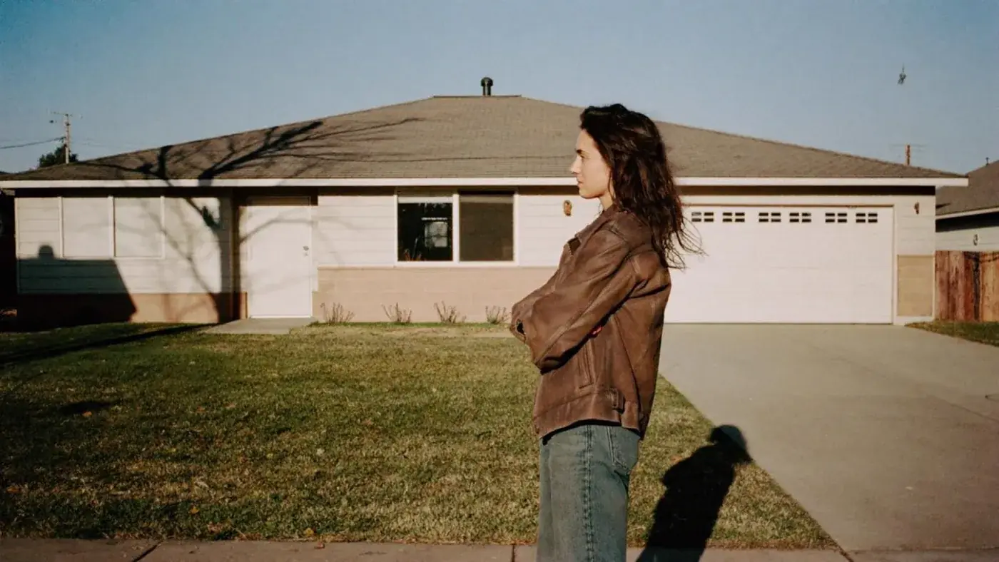 Before CreditHound: a woman standing on the sidewalk outside her single-story house, arms crossed, looking away