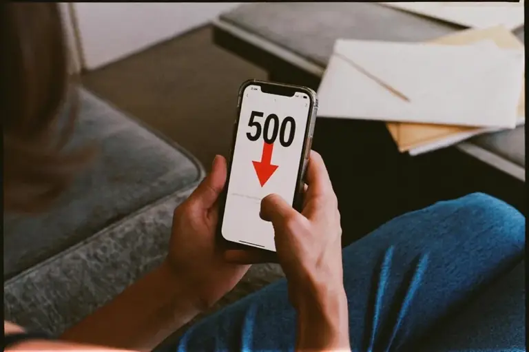 A person holding a phone showing a credit score of 500 with a red downward arrow